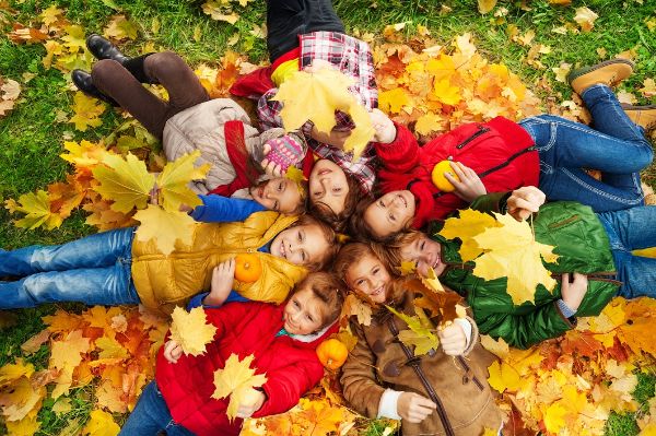 Gruppe von Kindern, die am Herbsttag mit Ahornblättern im Gras liegen