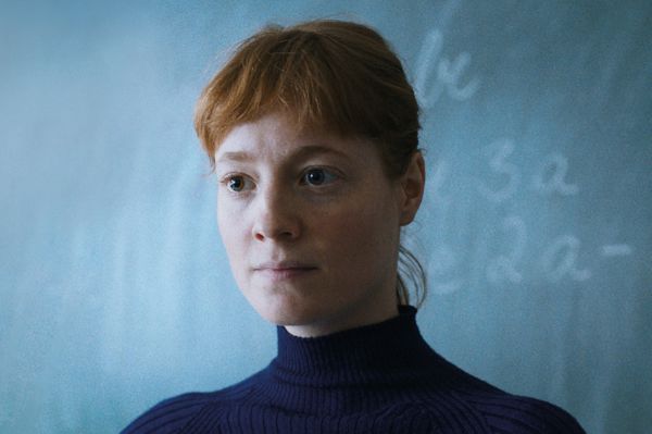 Portraitfoto einer rothaarigen-Frau, Lehrerin vor einer beschriebenen Klassentafel