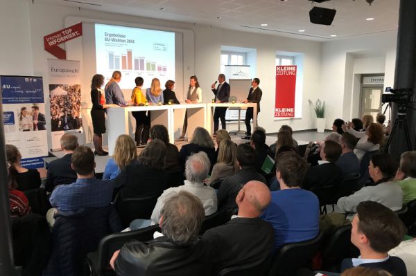 8 Personen bei einer Podiumsdiskussion vor Publikum 