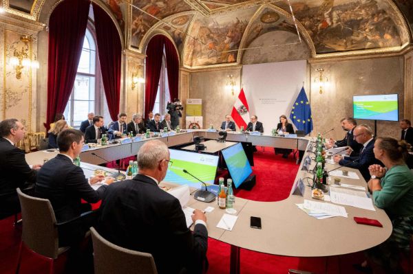 Mehrere Personen sitzen in einem Besprechungsraum an einem runden Tisch - roter Teppich, die Wände sind mit alten Gemälden verziert