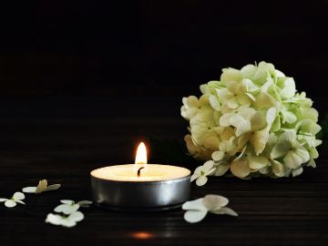 Trauerblumen und Kerze auf dunklem Hintergrund